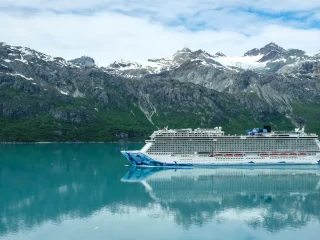 A cruise ship on calm green water below a glacier and snow covered peaks