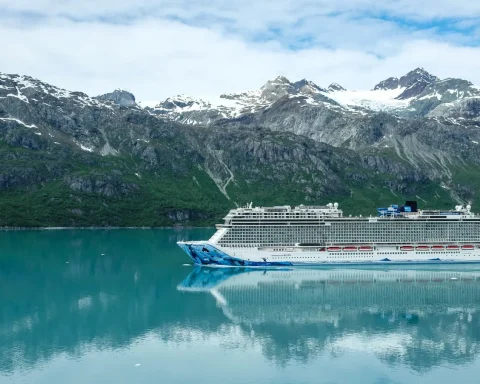 A cruise ship on calm green water below a glacier and snow covered peaks