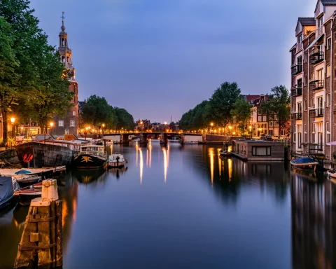 An Amsterdam canal at dusk with boats moored along the water
