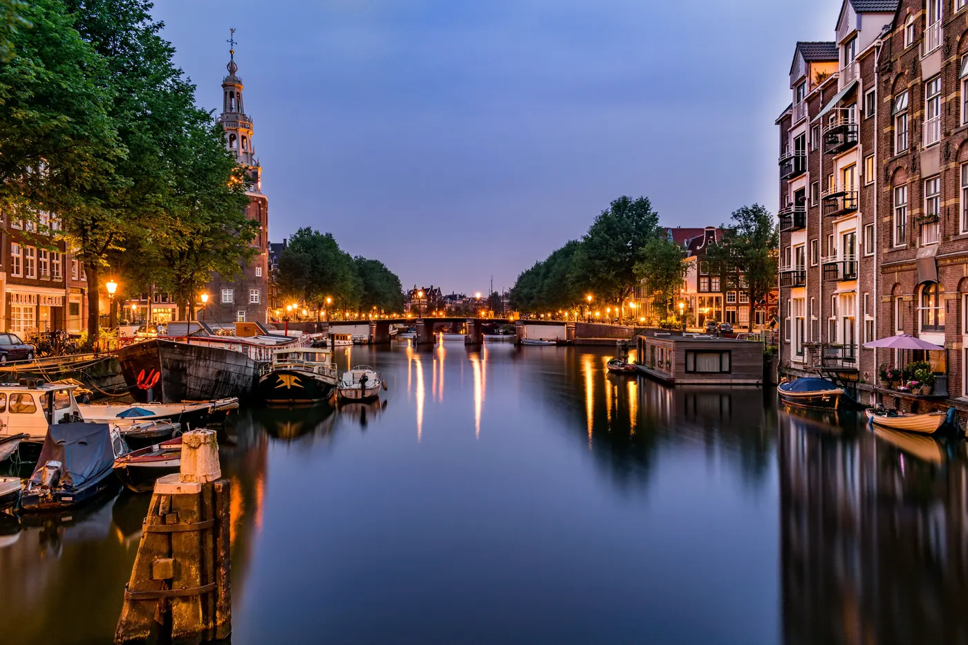 An Amsterdam canal at dusk with boats moored along the water