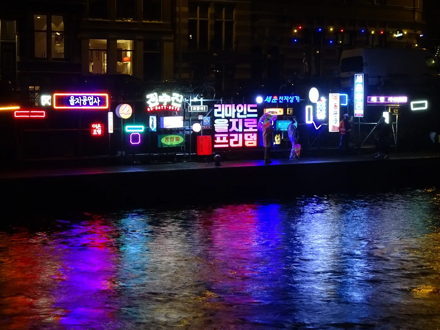 A neon light artwork glowing beside an Amsterdam canal during the Amsterdam Light Festival