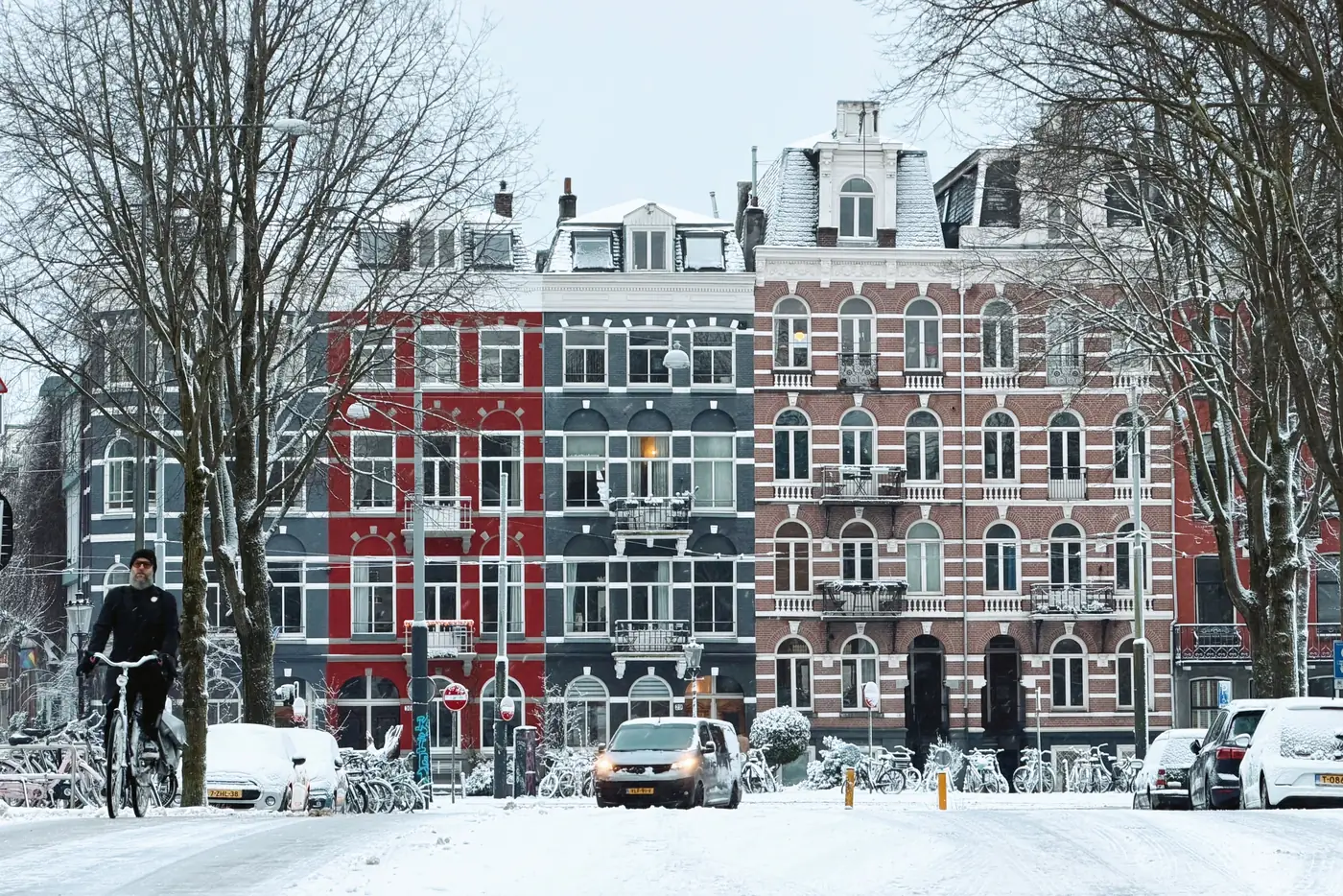 A cyclist riding past snow covered canal houses on an Amsterdam street in winter