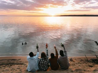 Friends sitting on a beach raising their drinks at sunset