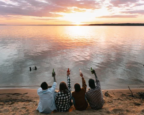 Friends sitting on a beach raising their drinks at sunset
