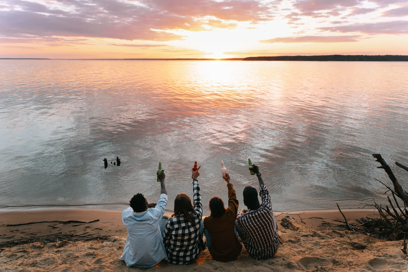 Friends sitting on a beach raising their drinks at sunset