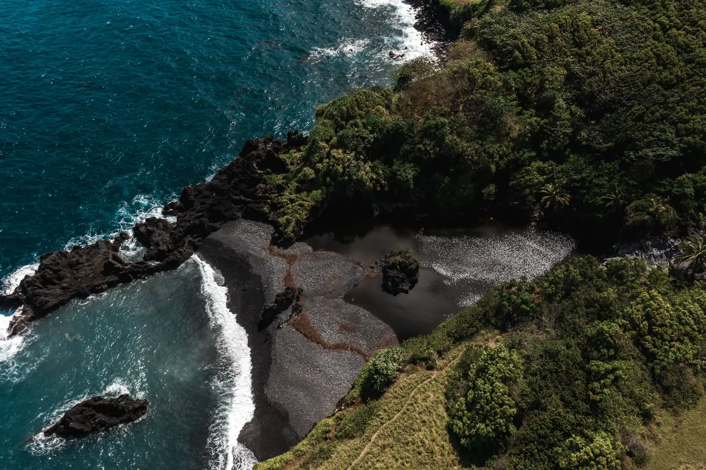 A black sand beach surrounded by green jungle near Hāna, Maui