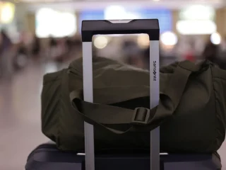 A green duffel bag sitting on a carry on suitcase handle in a busy airport terminal