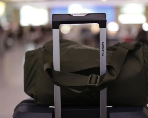 A green duffel bag sitting on a carry on suitcase handle in a busy airport terminal