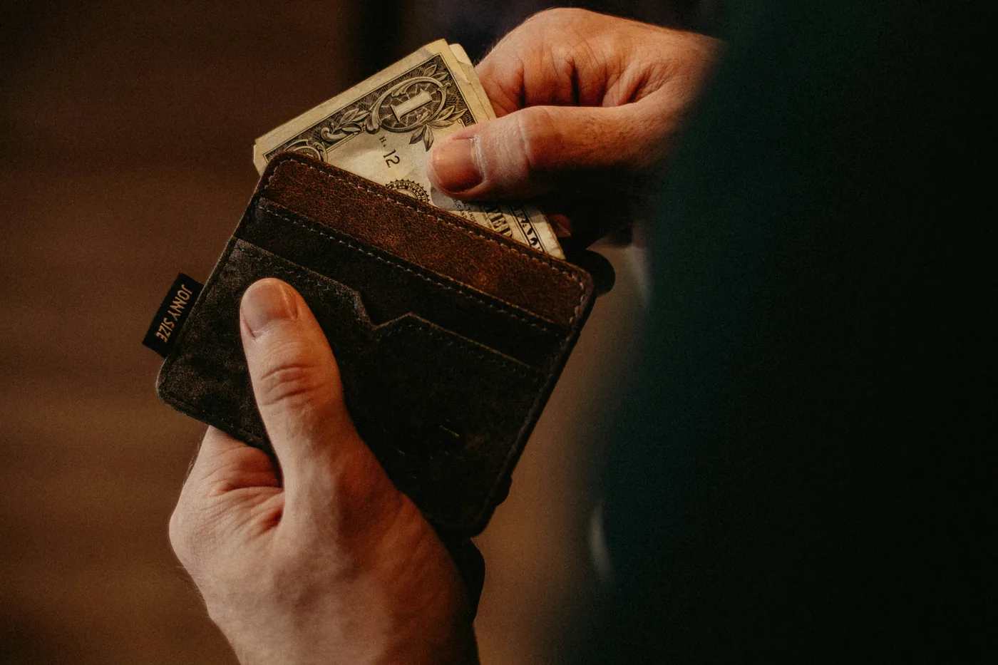 A hand tucking a US dollar bill into a leather card wallet