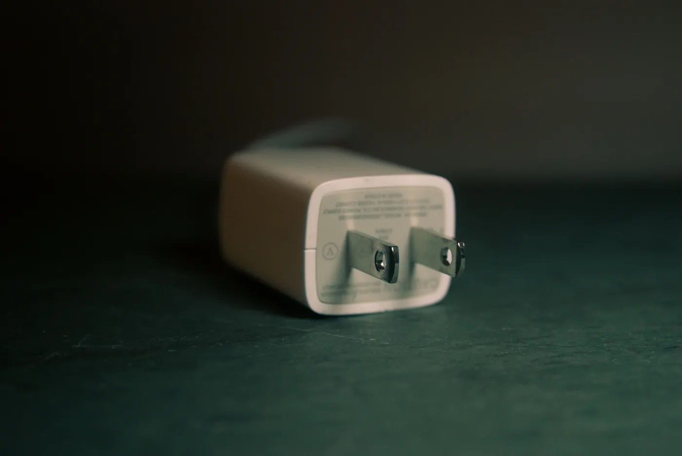 A small white wall charging plug on a dark table