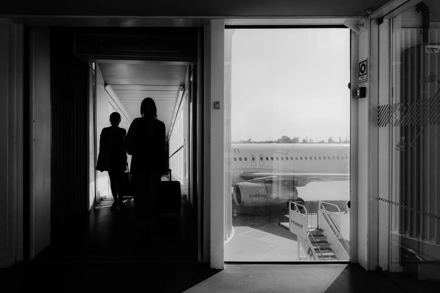 Travelers with carry on bags walking down a jet bridge toward a plane