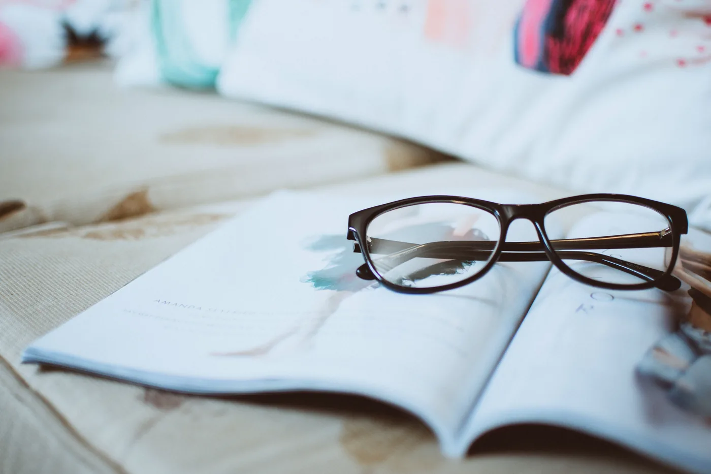 A pair of dark framed eyeglasses resting on an open magazine