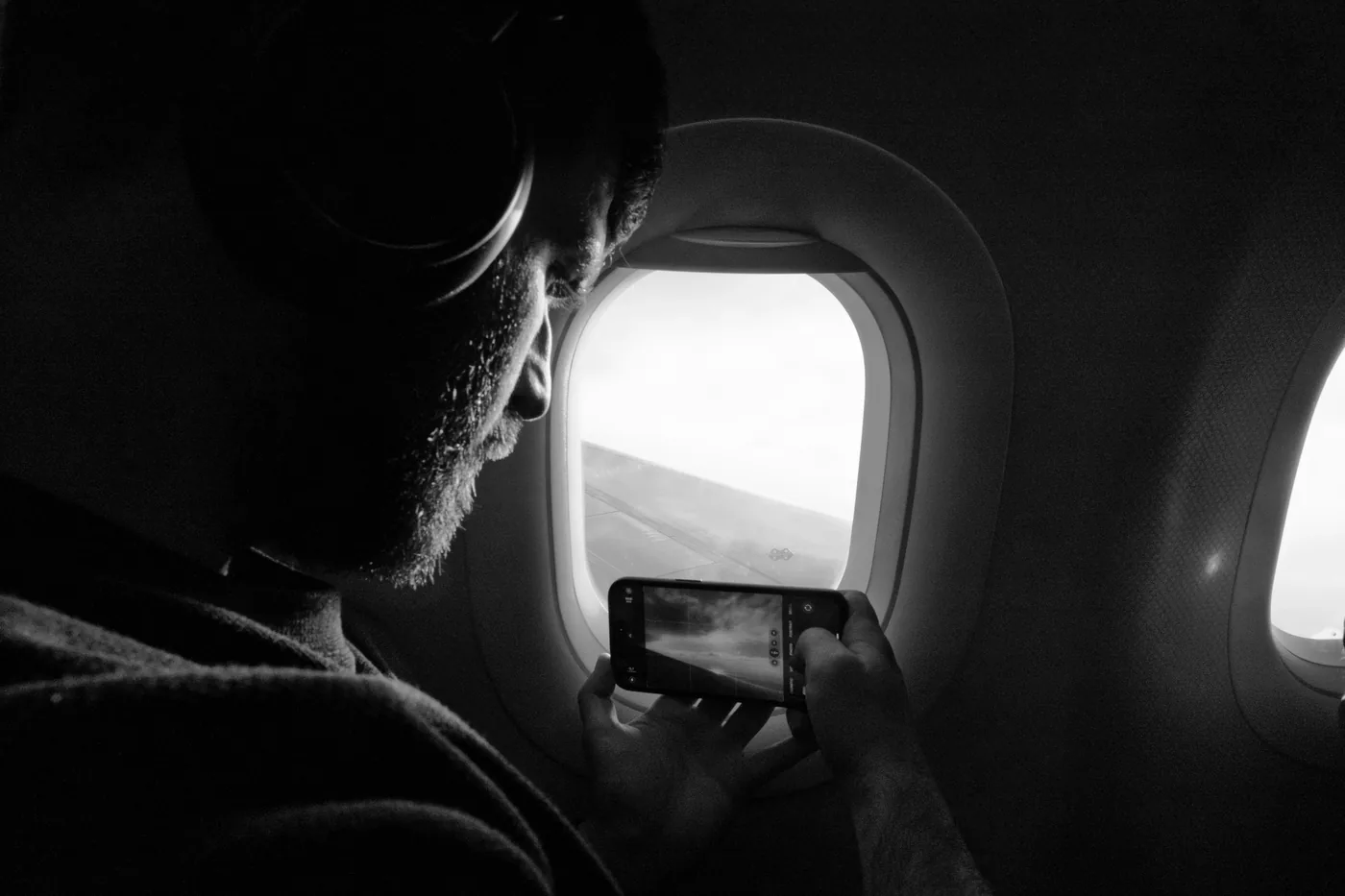 A passenger wearing headphones taking a photo out of an airplane window