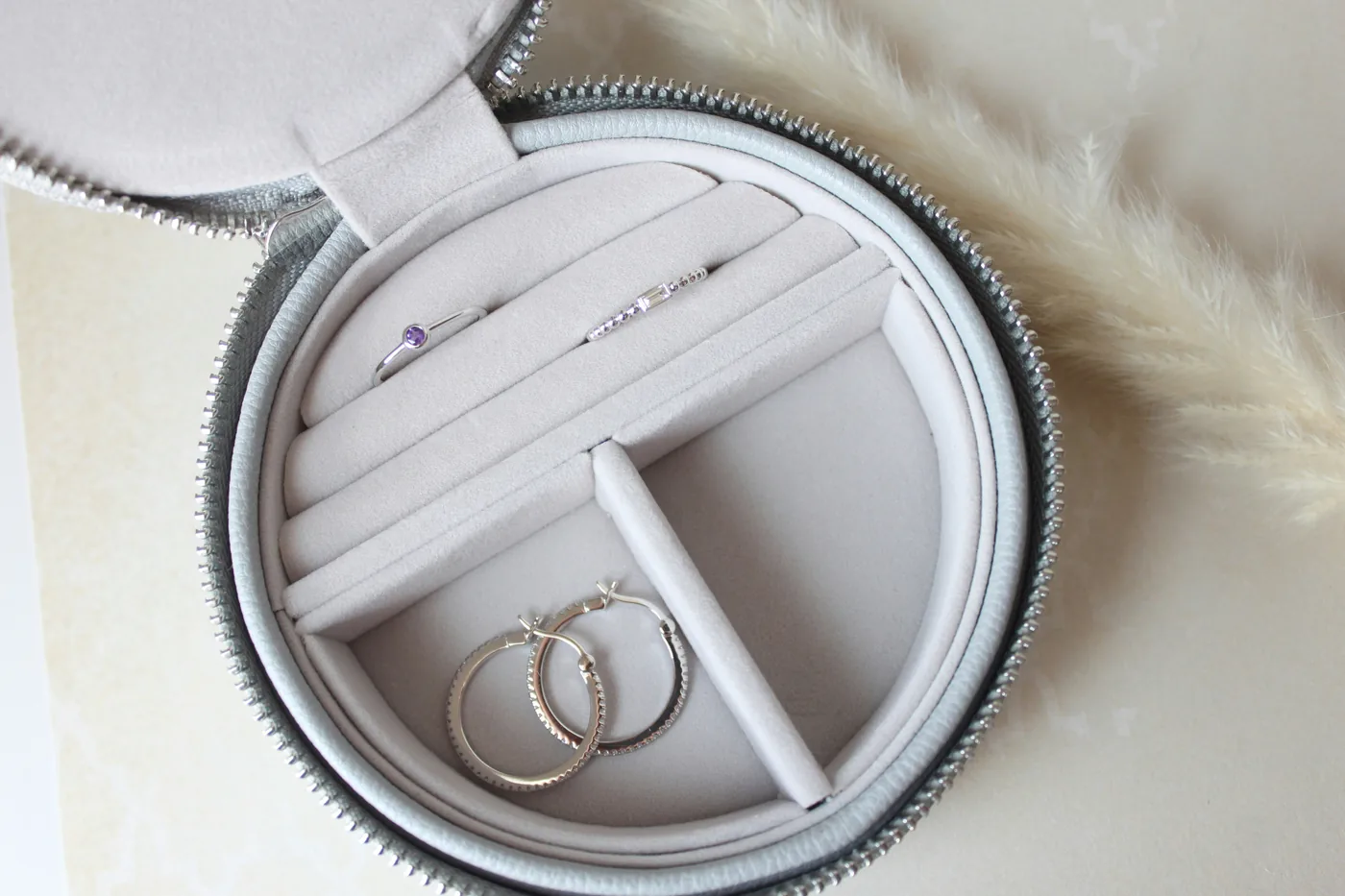 A small round travel jewelry case holding hoop earrings and rings
