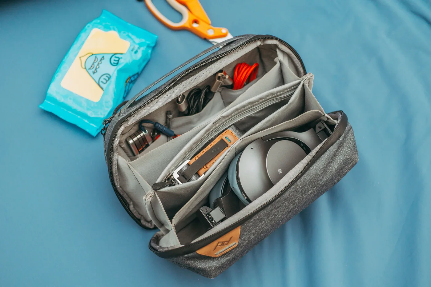 An open tech organizer pouch holding headphones and charging cables