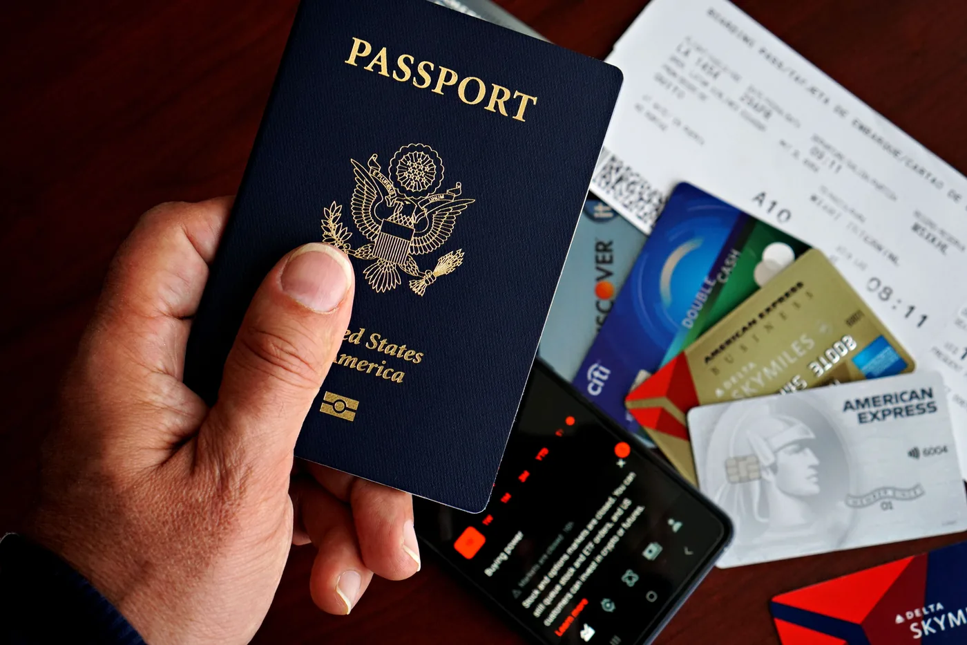 A hand holding a US passport over boarding passes and credit cards