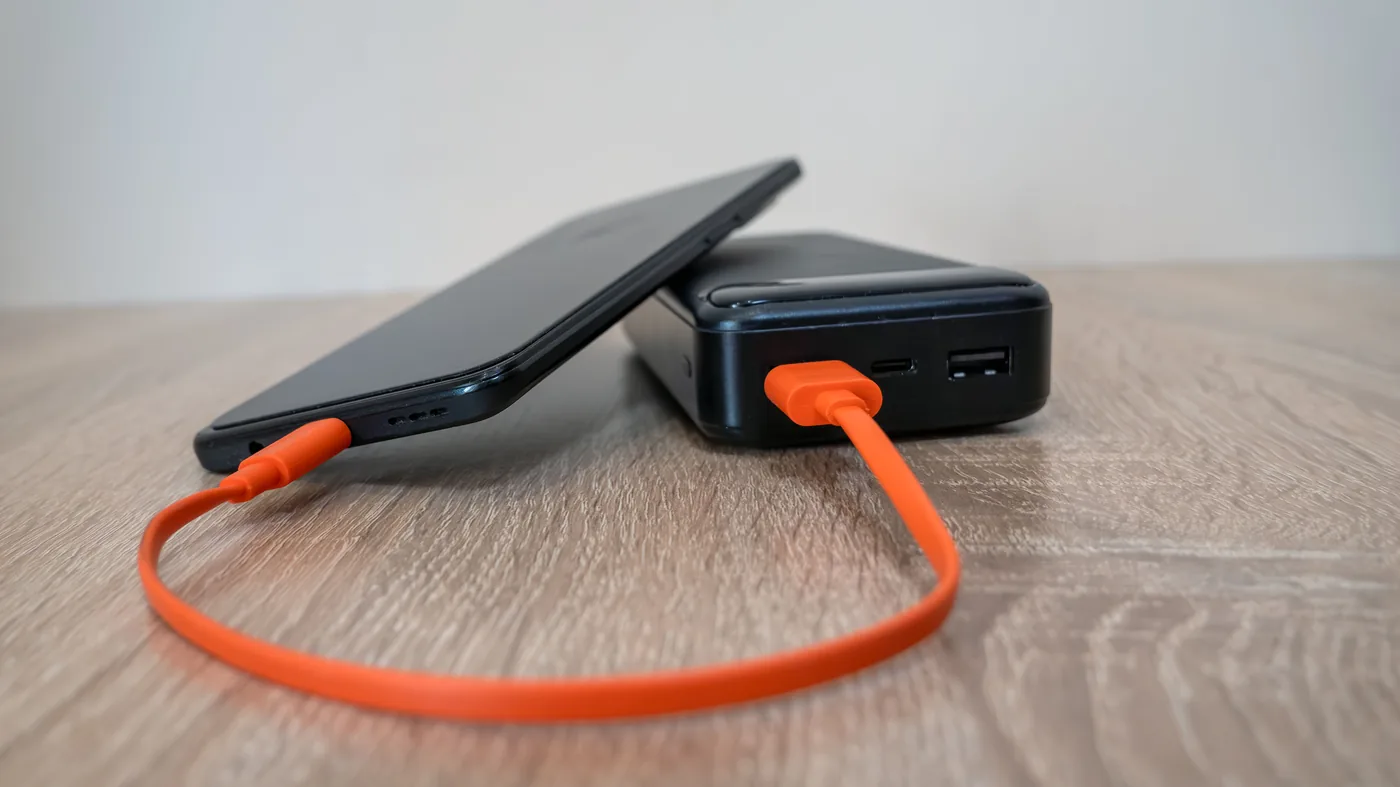 A phone charging from a portable power bank with a short orange cable