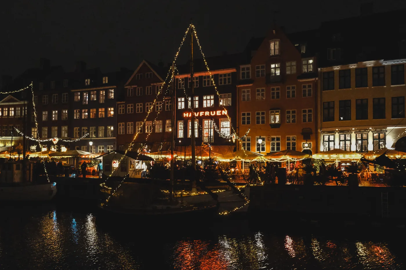 Holiday lights strung along the boats and harbor in Copenhagen at night