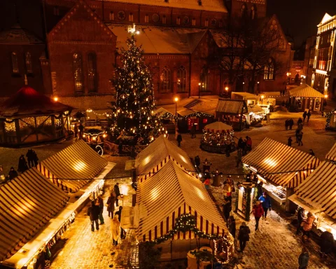 An overhead view of a snowy Christmas market lit up at night around a tall Christmas tree