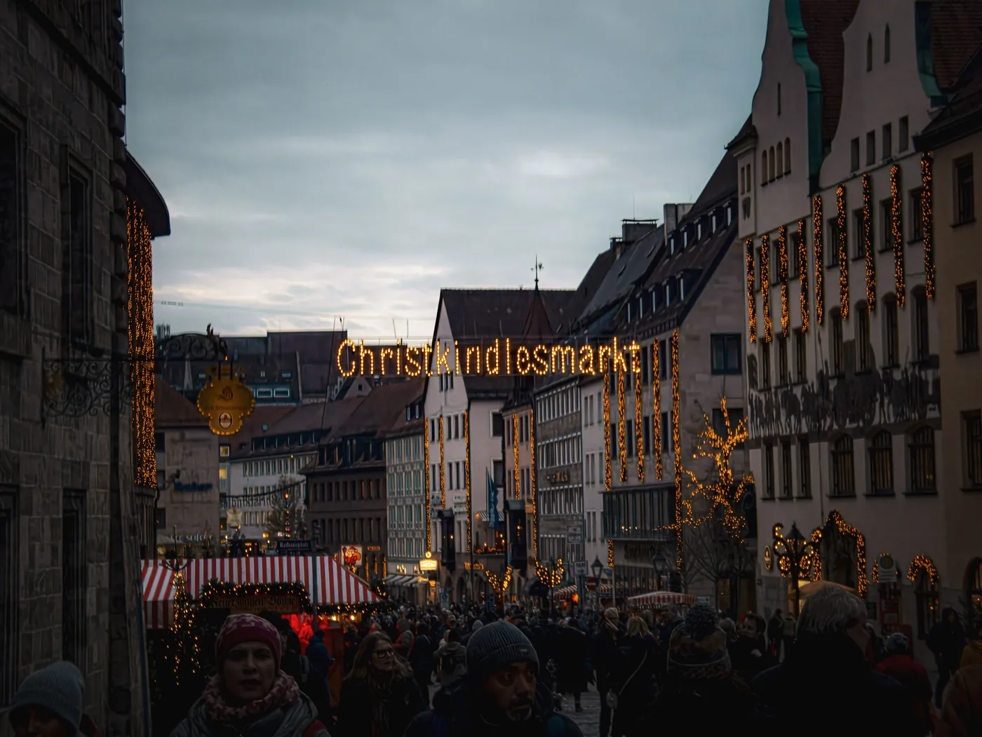 The Christkindlesmarkt sign lit up above a crowded street in Nuremberg at dusk