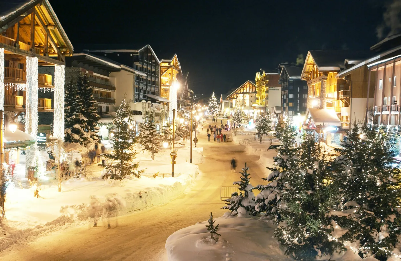 A snowy mountain village street lit up at night during the holidays