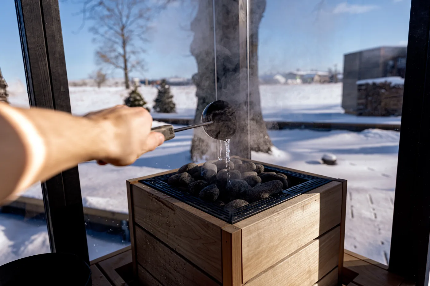 Water ladled over hot sauna stones with snow outside the window