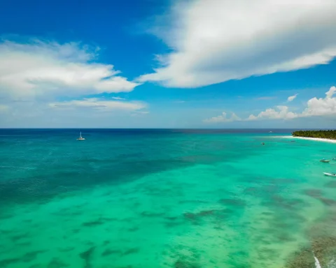 Aerial view of a turquoise lagoon with a sailboat anchored off a pale sand shore