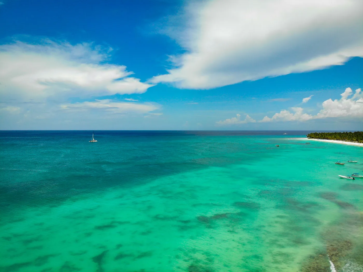 Aerial view of a turquoise lagoon with a sailboat anchored off a pale sand shore