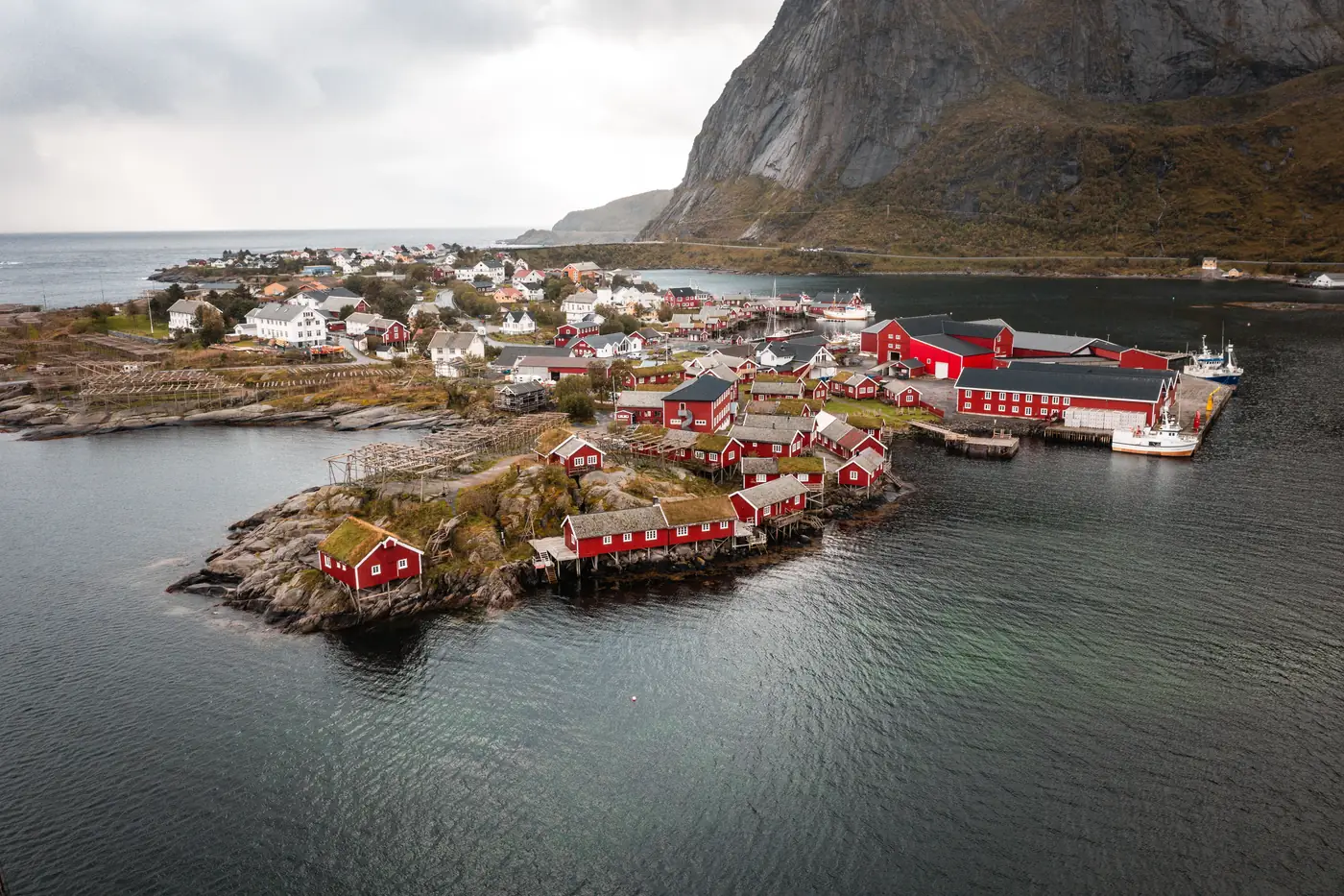 Red fishermen's cabins on a rocky islet below mountains in Lofoten, Norway