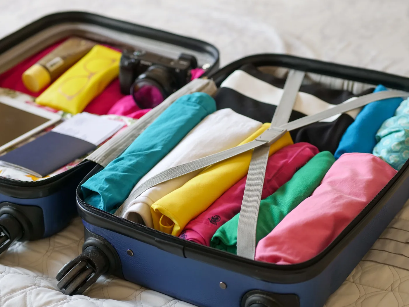 An open carry on suitcase packed with rolled clothes, a passport and a camera