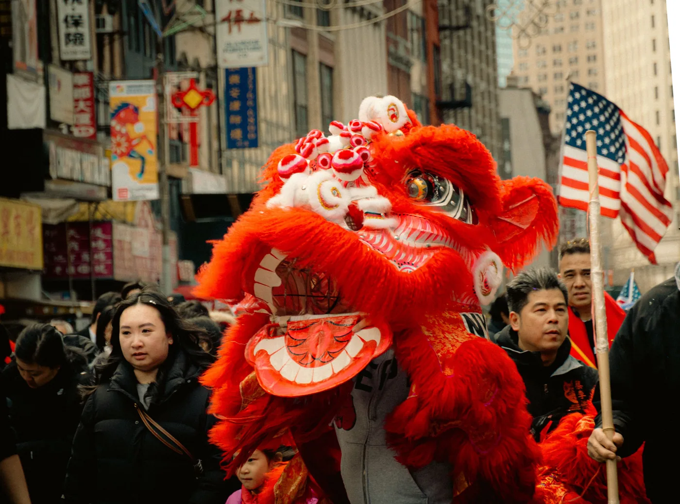 A red lion dance moving through a crowded Chinatown street