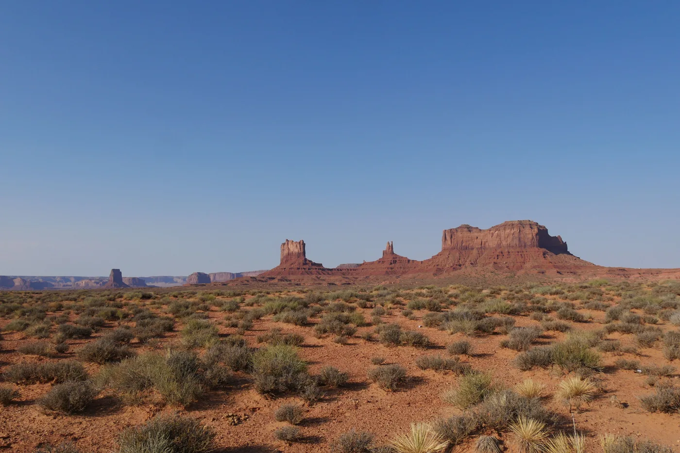 A wide view across the red desert floor to the buttes of Monument Valley