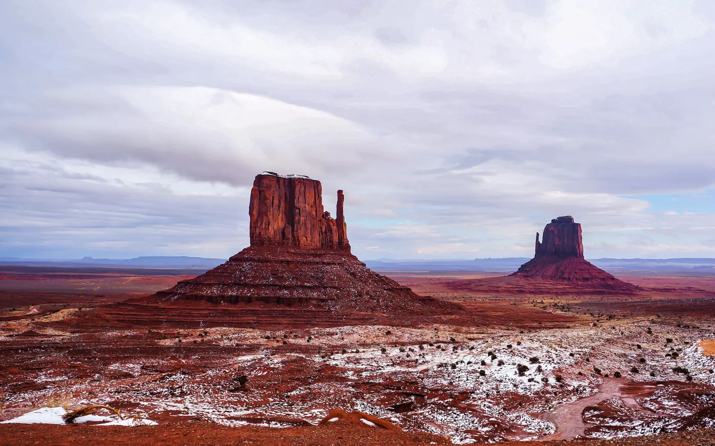 Snow lying on the red desert floor beneath the buttes of Monument Valley