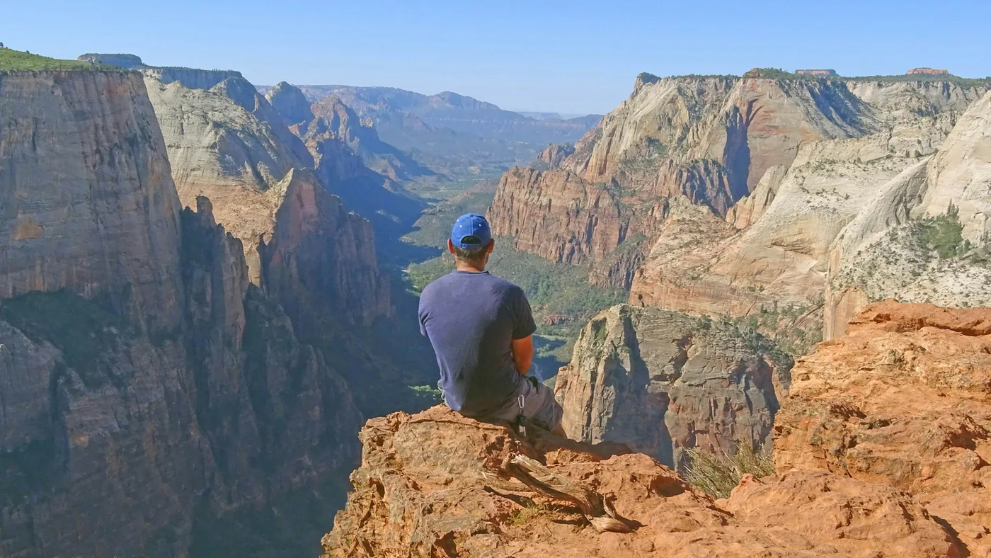 A hiker sitting at a high overlook above Zion Canyon
