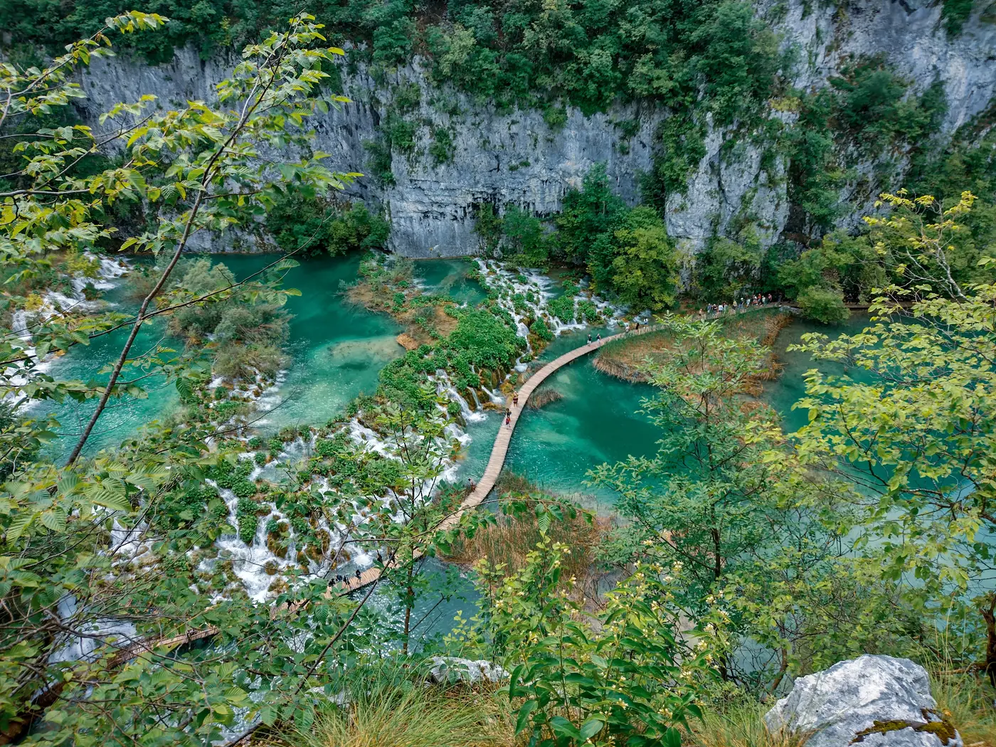 A wooden boardwalk crossing turquoise water at Plitvice Lakes