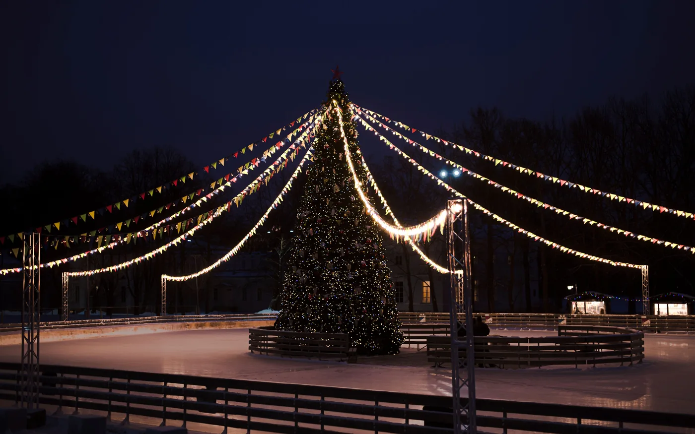 A lit Christmas tree at the center of an outdoor ice rink