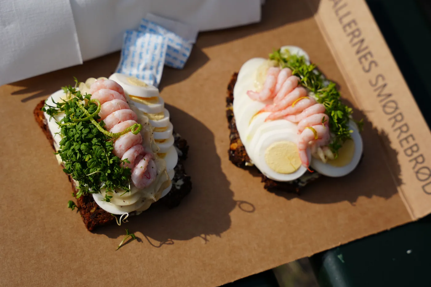Two shrimp and egg smørrebrød on rye bread in a Hallernes Smørrebrød box