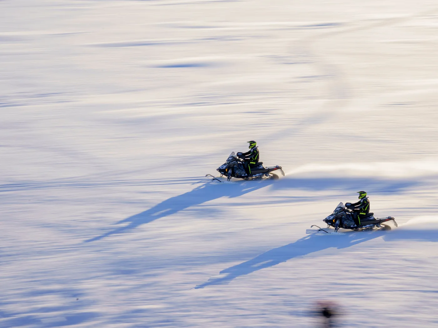 Two snowmobiles crossing a wide snowy field in Lapland, Finland