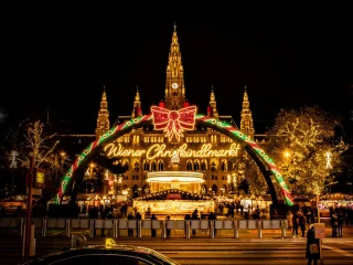 The illuminated Wiener Christkindlmarkt arch in front of Vienna's lit town hall at night