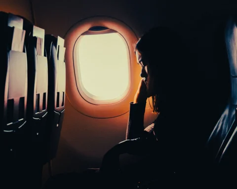 A passenger silhouetted against a glowing airplane window at sunset