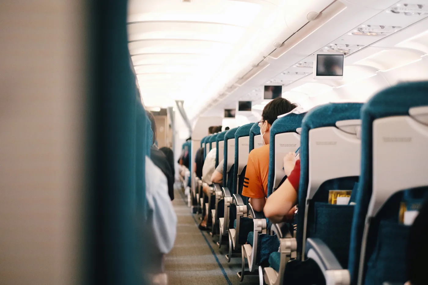 Passengers sitting in blue seats along an airplane aisle