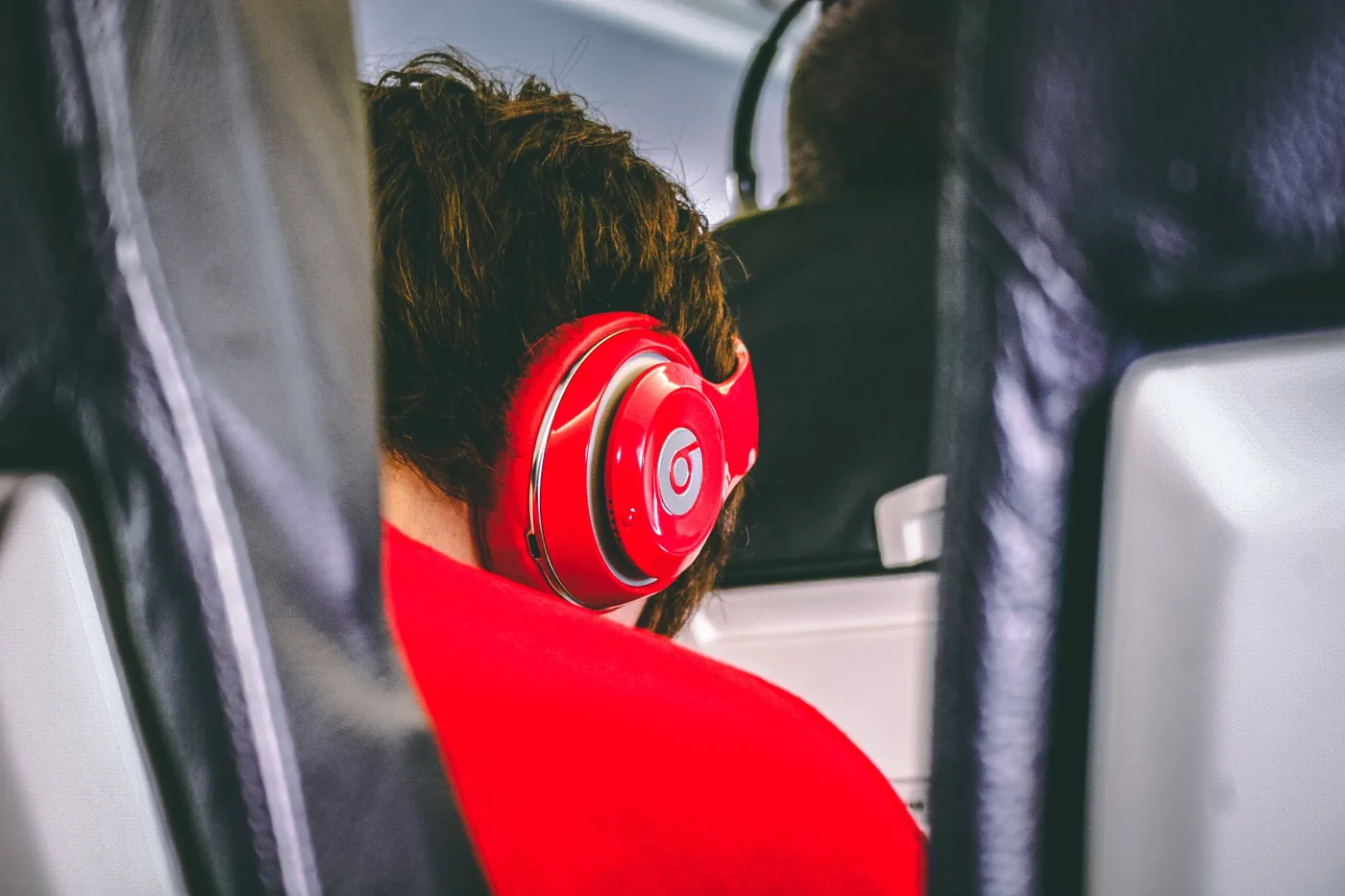 A passenger wearing red over ear headphones seen between airplane seats