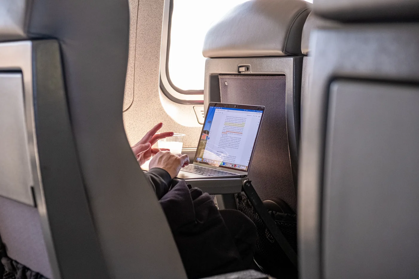 A laptop open on an airplane tray table beside the window