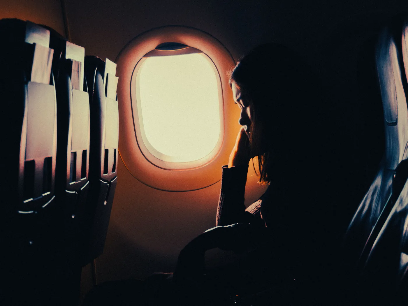A passenger silhouetted against a glowing airplane window at sunset