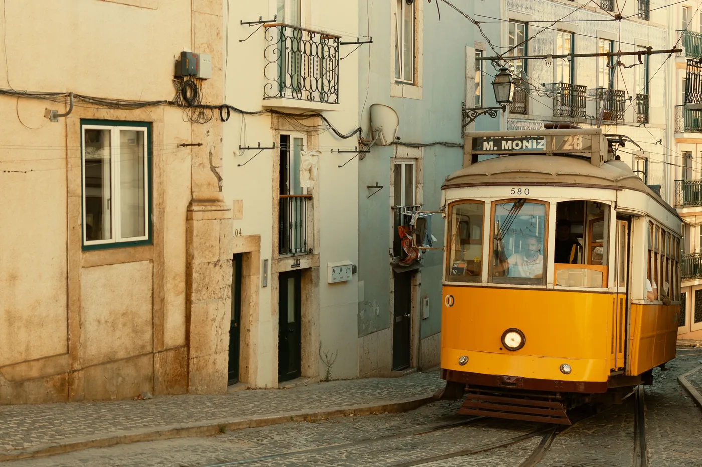 Yellow tram 28 on a narrow cobbled street in Lisbon