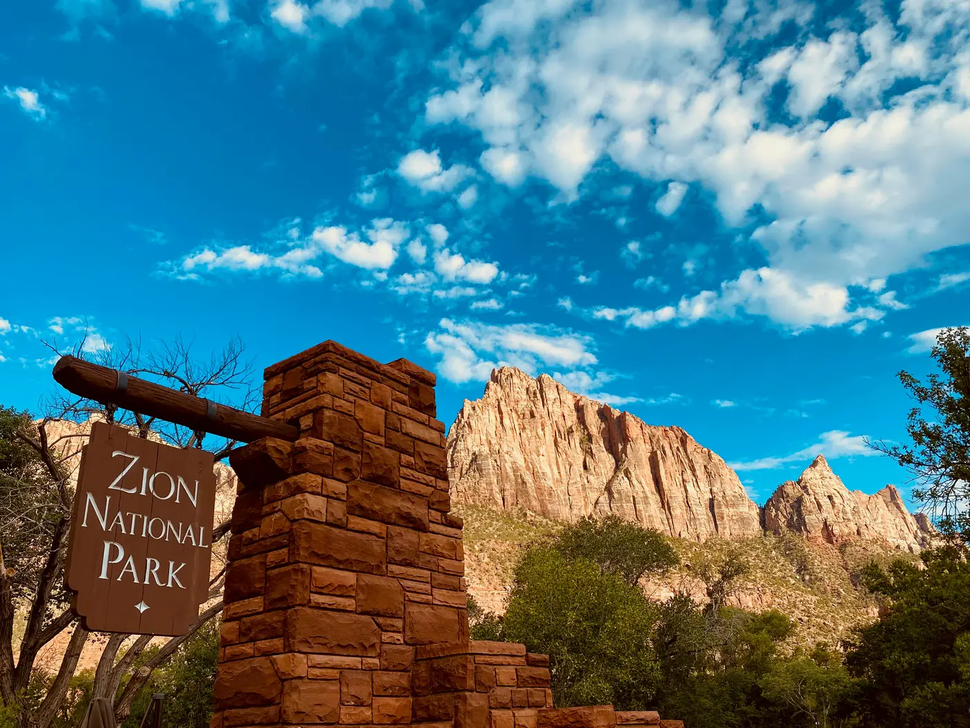 The stone Zion National Park entrance sign below the red cliffs