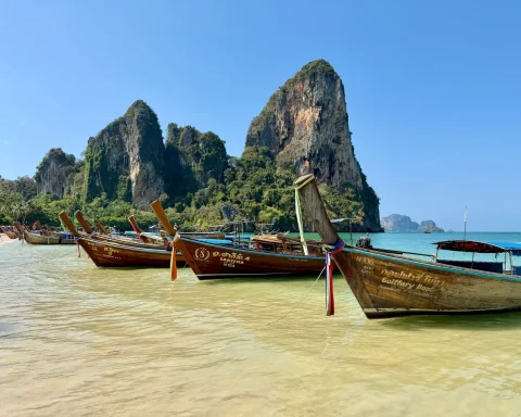 Longtail boats pulled up on Railay Beach under tall limestone cliffs in Krabi