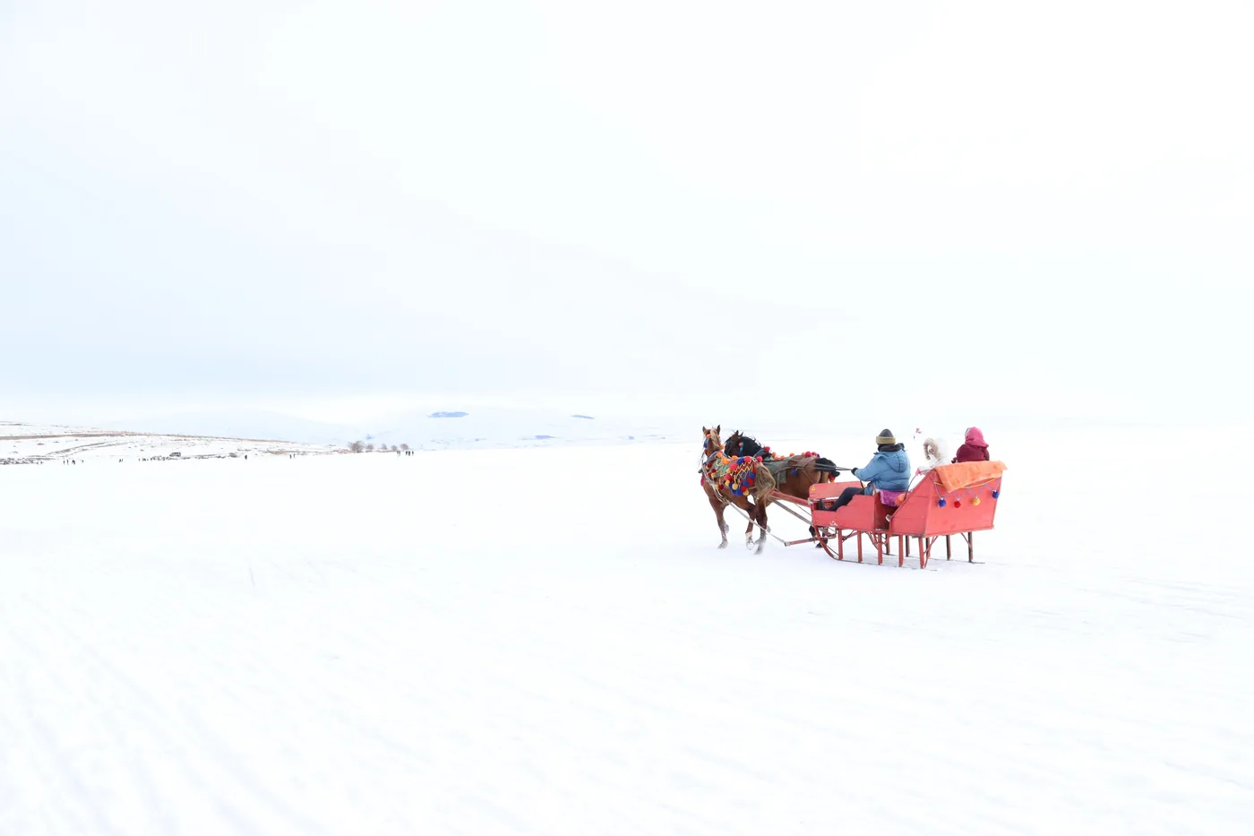 A red horse drawn sleigh crossing a wide snowy field