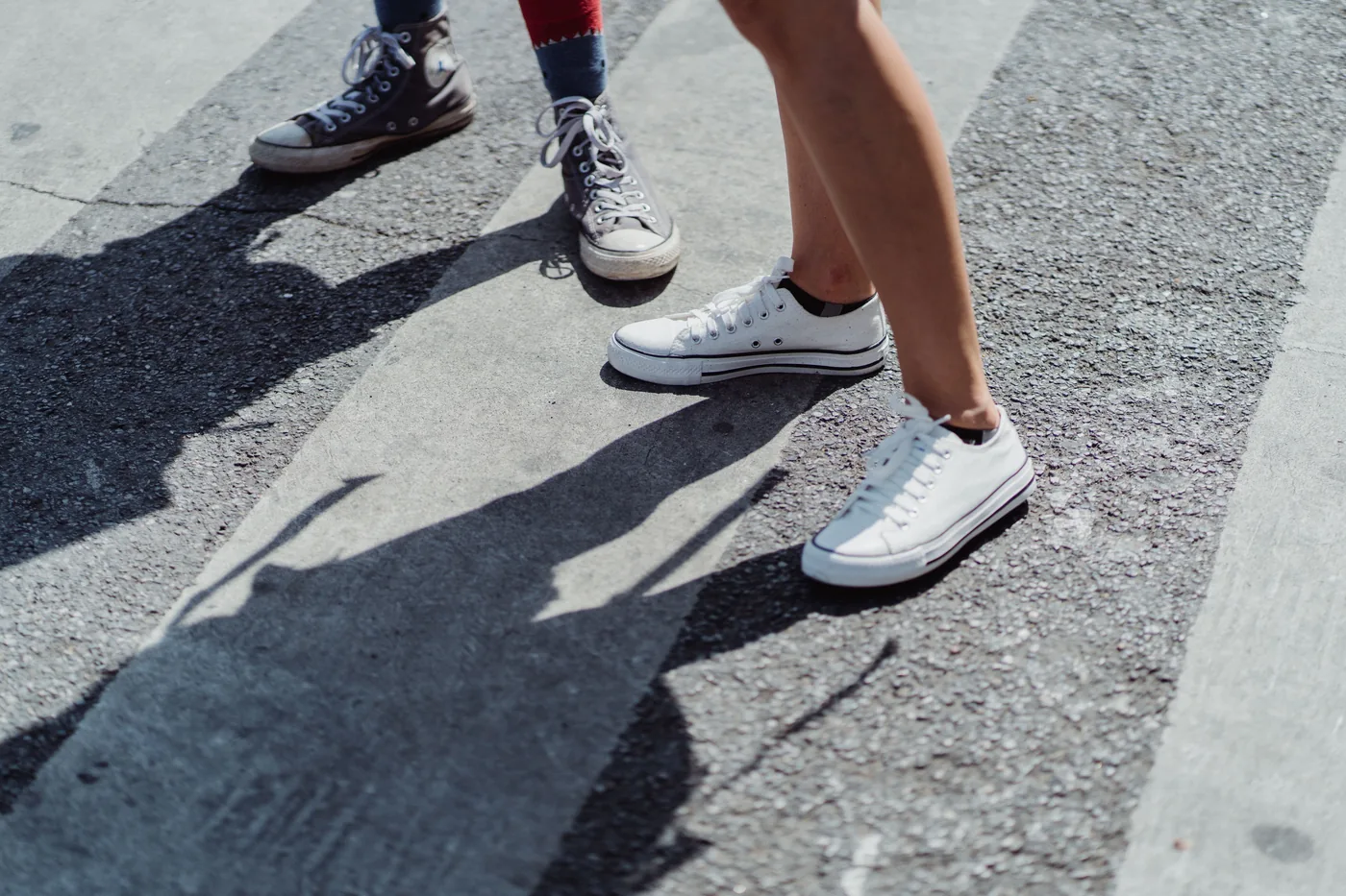 Two people in sneakers crossing a sunny street