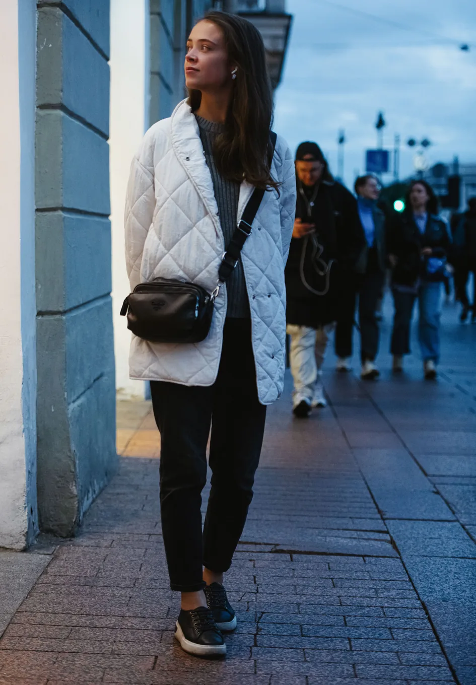 A woman walking down a city street with a small crossbody bag